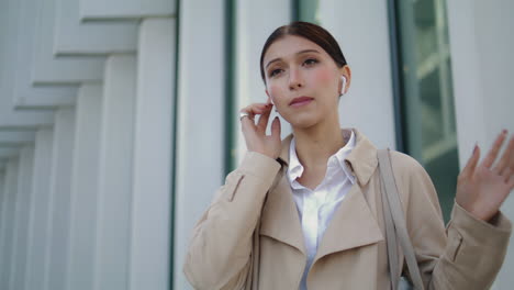 Girl-communicating-wireless-earbuds-standing-city-street-alone-close-up.