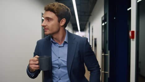Relaxed-employee-holding-coffee-cup-closeup.-Company-ceo-walking-hallway-resting