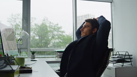 Office-worker-leaning-chair-at-glass-workplace.-Thoughtful-man-taking-break