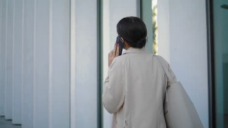 Back-view-businesswoman-calling-phone-walking-near-office-building-vertically