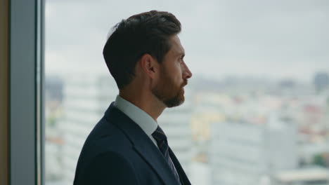 Man-standing-office-window-watching-at-city-view-close-up.-Serious-businessman.