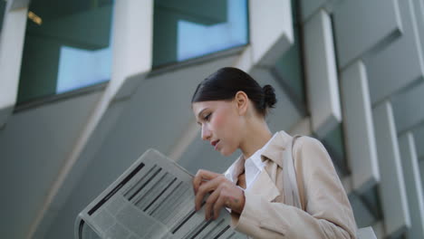 Woman-turning-newspaper-pages-standing-outdoors-close-up.-Businesswoman-reading