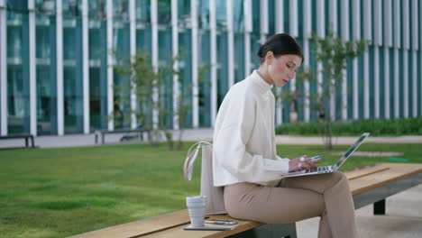 Mujer-De-Negocios-Trabajando-Remotamente-En-Un-Banco-Sentado-En-Una-Computadora-Portátil-Escribiendo-Verticalmente-Un-Informe