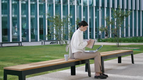 Student-writing-diploma-laptop-sitting-bench-near-university.-Girl-work-synopsis