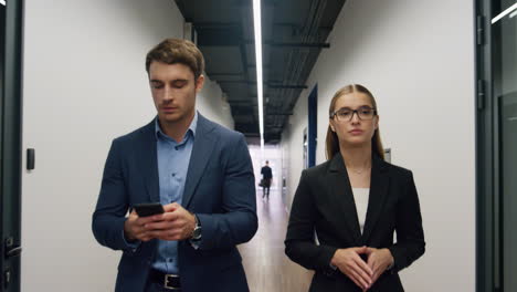 Business-partners-walking-office-together.-Focused-manager-texting-smartphone