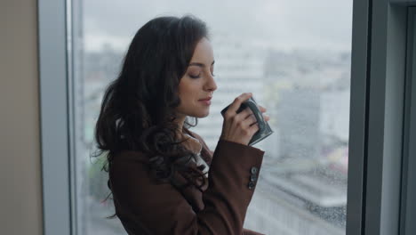 Closeup-woman-drinking-coffee-looking-on-city-from-office-window.-Girl-resting.