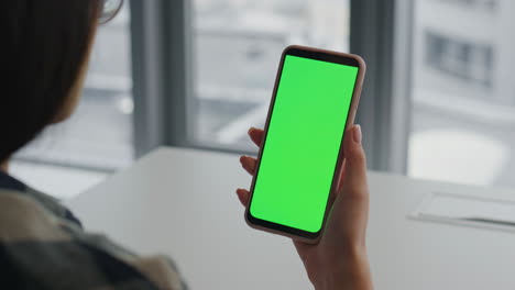 Lady-hands-holding-greenscreen-smartphone-indoors.-Trader-reading-cellphone