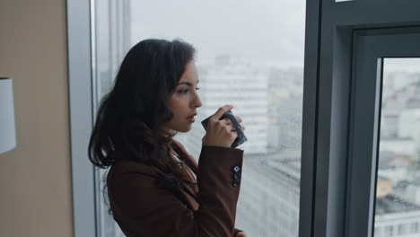 Woman-manager-drinking-tea-looking-on-cityscape-from-office-window-close-up.