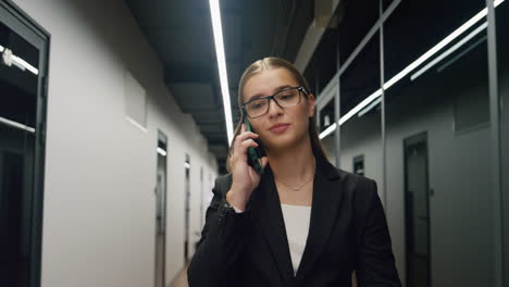Young-businesswoman-making-call-walking-contemporary-business-center-closeup.