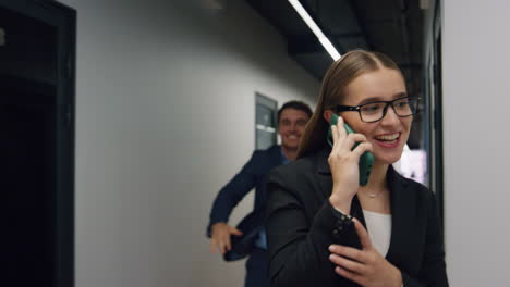 Office-girl-talking-mobile-phone-going-hall.-Handsome-man-colleague-embracing
