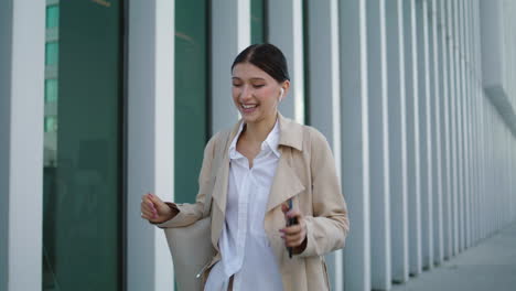 Woman-calling-wireless-earbuds-walking-city-street.-Girl-talking-by-smartphone.