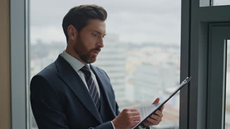 Businessman-checking-corporate-papers-standing-at-office-window-close-up.