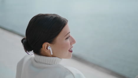 Side-view-woman-calling-by-wireless-earbuds-sitting-alone-close-up.-Lady-talking