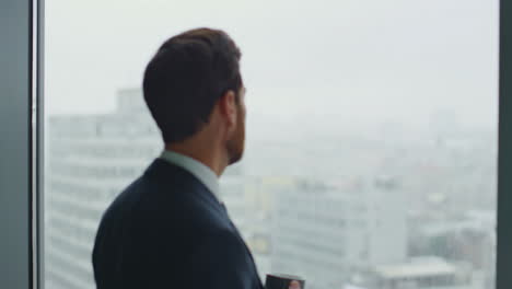 Serious-director-drinking-coffee-looking-on-office-window-cityscape-close-up.