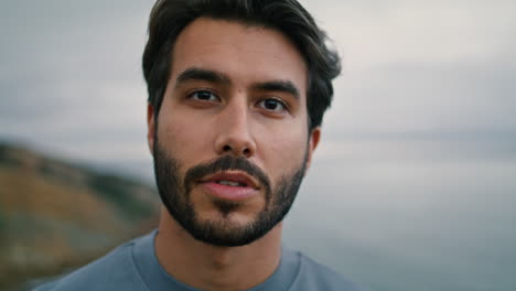 Man-looking-camera-cloudy-seascape-on-backdrop-closeup.-Portrait-of-handsome-guy