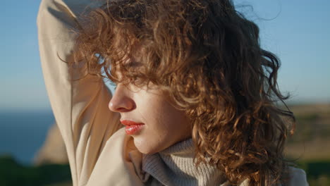 Girl-closing-eyes-sunlight-vertical-closeup.-Serene-woman-touching-curly-hair