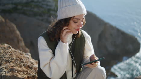 Relaxed-girl-listen-music-on-ocean-cliff-vertical.-Stress-free-traveler-resting