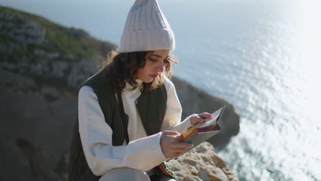 Calm-girl-enjoying-book-at-ocean-cliff-vertical.-Focused-traveler-rest-mountain