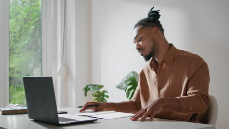 Beschäftigter-Typ,-Der-In-Einem-Hellen-Büro-Daten-Auf-Papier-Schreibt.-Afro-Mann-Studiert-Und-Schaut-Auf-Laptop
