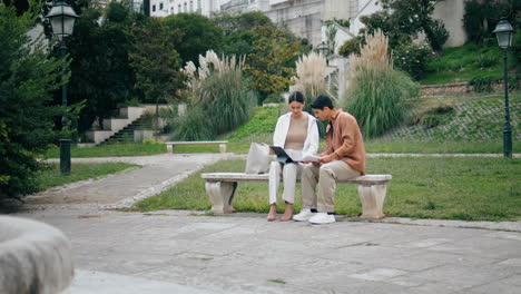 College-students-learning-tablet-on-bench-vertically.-Couple-working-green-park