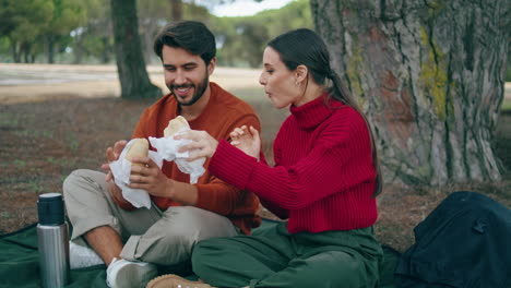 Couple-eating-romantic-picnic-in-forest.-Young-pair-tasting-food-on-blanket.