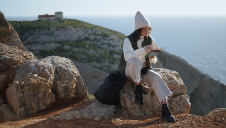 Romantic-girl-reading-book-on-rocky-mountain-vertical.-Tourist-rest-ocean-cliff