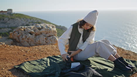 Picnic-girl-pouring-coffee-on-cliff-edge-vertical.-Carefree-tourist-rest-ocean