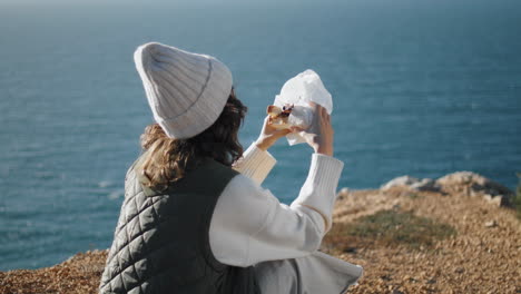 Travel-girl-eating-sandwich-at-rocky-cliff-edge.-Vertically-tourist-take-break