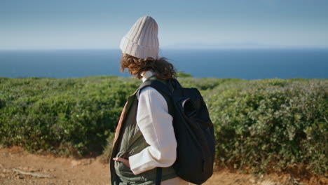 Girl-traveling-backpack-alone-at-ocean-view.-Thinking-tourist-walking-rocky