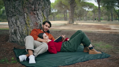 Tender-couple-lying-blanket-at-romantic-forest-picnic.-Man-reading-loud-book