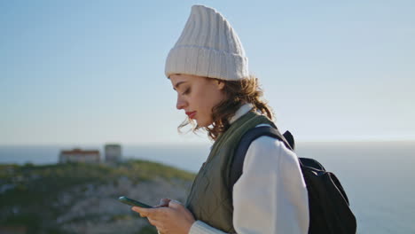 Wanderndes-Mädchen,-Das-Mit-Dem-Smartphone-Eine-SMS-Schreibt,-Mit-Blick-Auf-Das-Meer-Und-Die-Berge.-Lächelnder-Tourist-Beim-Wandern
