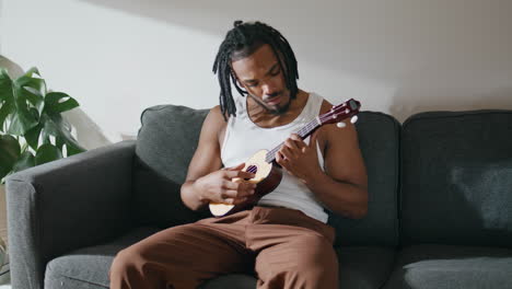 Contemporary-man-playing-ukulele-closeup.-Dreadlocks-guy-engaging-in-guitar