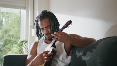 Focused-musician-playing-guitar-domestic-place.-Satisfied-man-enjoying-ukulele
