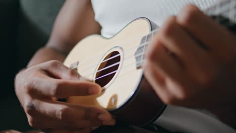 Man-hands-playing-ukulele-indoors.-Unknown-musician-touching-strings-at-home