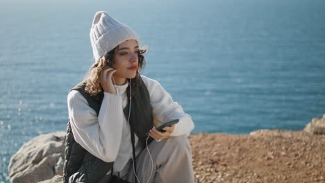 Pretty-girl-listening-online-music-on-cliff-vertical.-Serene-woman-relax-ocean