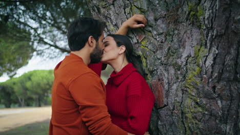 Lovely-couple-kissing-park-leaning-at-tree-closeup.-Family-pair-standing-hugging
