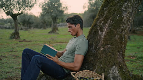 Interested-gardener-reading-storybook-nature-closeup.-Man-leaning-tree-vertical