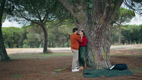 Loving-couple-enjoy-weekend-on-nature.-Happy-tourists-standing-hugging-near-tree