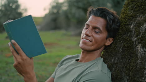 Smiling-guy-holding-book-sunset-park-portrait.-Man-looking-camera-reading-novel