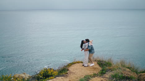 Funny-couple-dancing-sea-coast-hill-cloudy-evening.-Pair-hugging-on-ocean-shore.