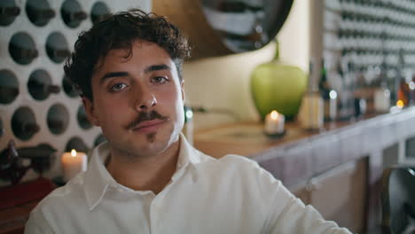Portrait-man-sitting-restaurant-in-white-shirt.-Brunet-looking-camera-close-up.