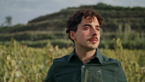 Man-winegrower-looking-vineyard-holding-glass-goblet-with-white-wine-close-up.