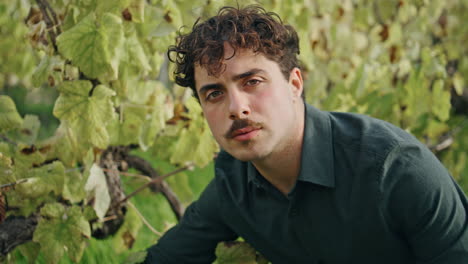 Happy-young-winegrower-looking-camera-at-grape-plantation-vertically-closeup