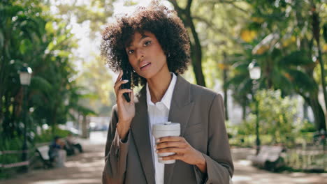 Businesswoman-calling-standing-park-with-coffee-close-up.-Curly-girl-using-phone