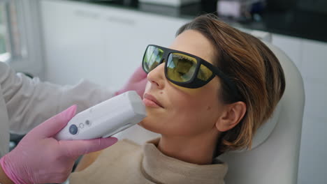 Woman-having-laser-facial-procedure-lying-couch-cosmetology-clinic-close-up.