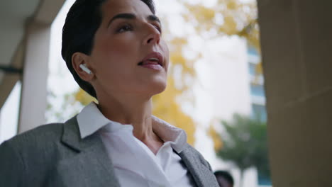 Walking-businesswoman-listening-music-in-earpods-closeup.-Relaxed-manager-drink