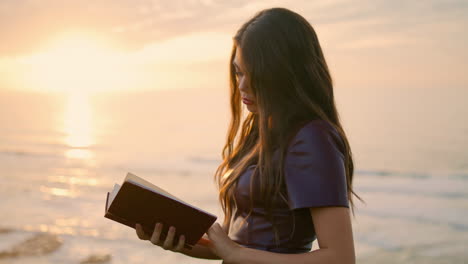 Girl-reading-book-sunset-close-up.-Brunette-holding-foliant-standing-at-seashore