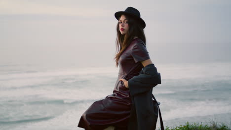 Model-posing-nature-twilight-wearing-stylish-hat.-Woman-sitting-at-stormy-sea