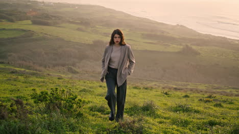 Attractive-girl-climbing-hill-covered-green-grass.-Woman-walking-near-calm-ocean