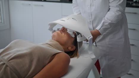 Kosmetikerin-Macht-Hautbehandlung-Und-Schaltet-LED-Maske-In-Schönheitsklinik-Ein,-Nahaufnahme